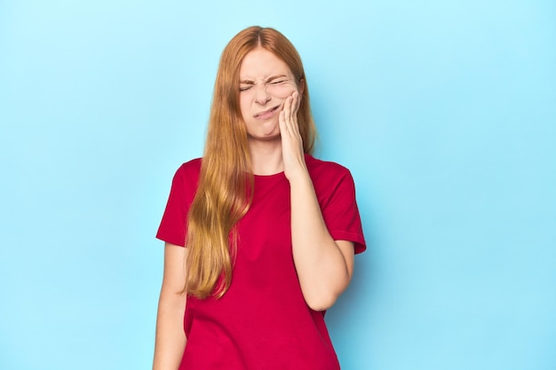 Foto jovem ruiva sobre fundo azul com forte dor nos dentes, dor molar