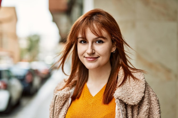 Jovem ruiva sorrindo feliz de pé na cidade