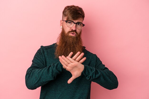 Jovem ruivo caucasiano com barba comprida isolado em um fundo rosa fazendo um gesto de negação