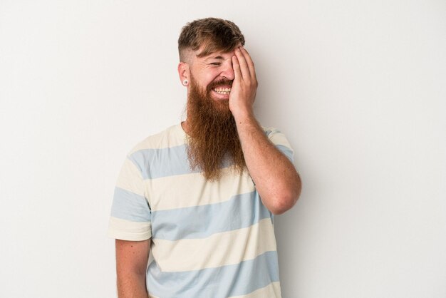 Jovem ruivo caucasiano com barba longa, isolado no fundo branco, rindo de emoção feliz, despreocupada e natural.