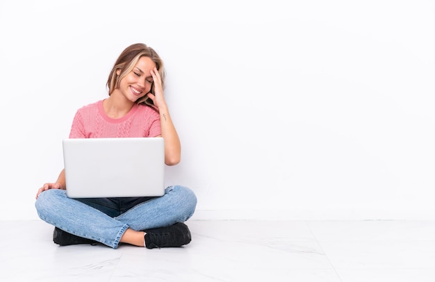 Jovem russa com um laptop sentado no chão isolado no fundo branco rindo
