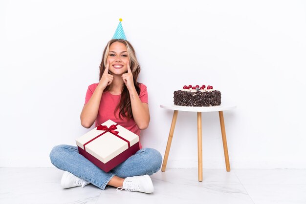 Jovem russa comemorando um aniversário sentada no chão isolada no fundo branco sorrindo com uma expressão feliz e agradável