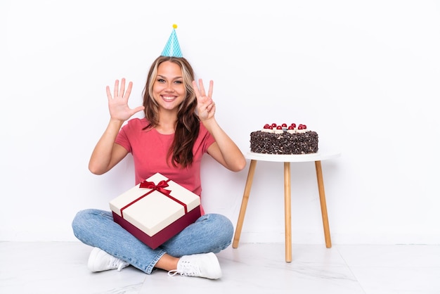 Jovem russa comemorando um aniversário sentado no chão isolado no fundo branco contando oito com os dedos