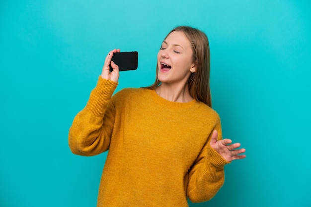 Jovem russa isolada em fundo azul usando telefone celular e cantando