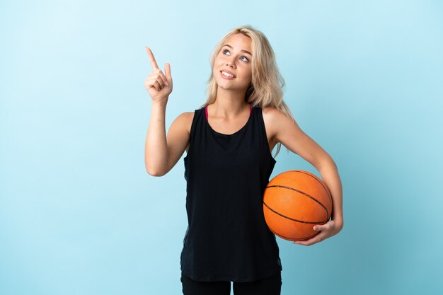 Jovem russa jogando basquete isolada em um fundo azul apontando com o dedo indicador uma ótima ideia
