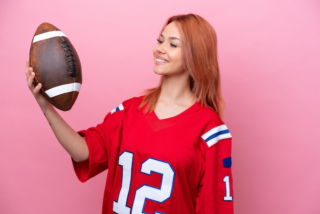 Jovem russa jogando rugby isolada em fundo rosa com expressão feliz