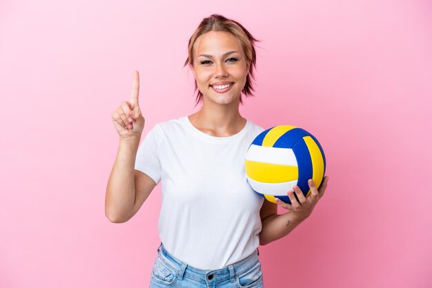 Jovem russa jogando vôlei isolada em fundo rosa mostrando e levantando um dedo em sinal do melhor