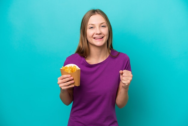 Jovem russa pegando batatas fritas isoladas em fundo azul comemorando uma vitória na posição de vencedor