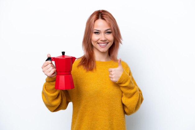 Jovem russa segurando cafeteira isolada em fundo branco com polegares para cima porque algo bom aconteceu