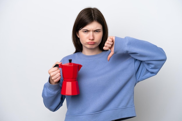 Jovem russa segurando o bule de café isolado no fundo branco, mostrando o polegar para baixo com expressão negativa