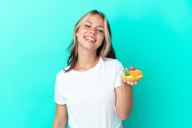 Jovem russa segurando um doce de fruta isolado no fundo azul rindo