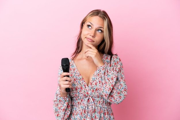Jovem russa segurando um microfone isolado em fundo rosa com dúvidas