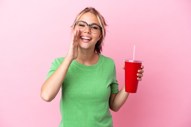 Jovem russa segurando um refresco isolado no fundo rosa gritando com a boca aberta