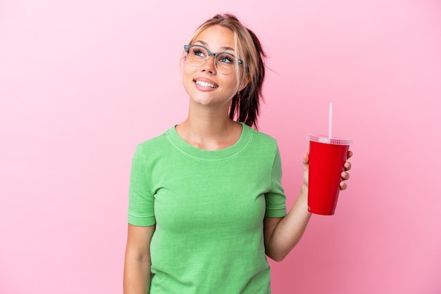 Jovem russa segurando um refresco isolado no fundo rosa pensando em uma ideia enquanto olha para cima