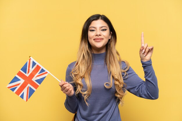 Jovem russa segurando uma bandeira do Reino Unido isolada em um fundo amarelo apontando uma ótima ideia