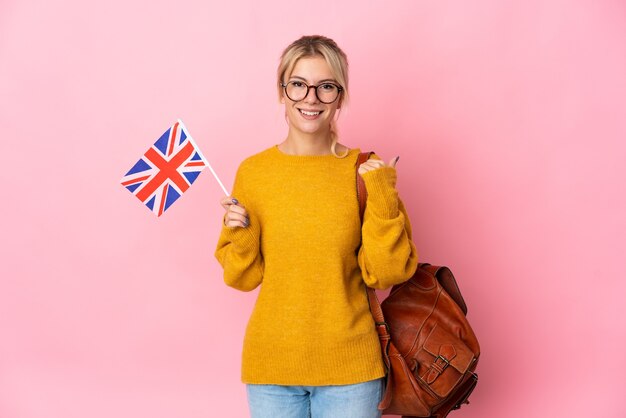 Jovem russa segurando uma bandeira do Reino Unido isolada em um fundo rosa apontando para o lado para apresentar um produto