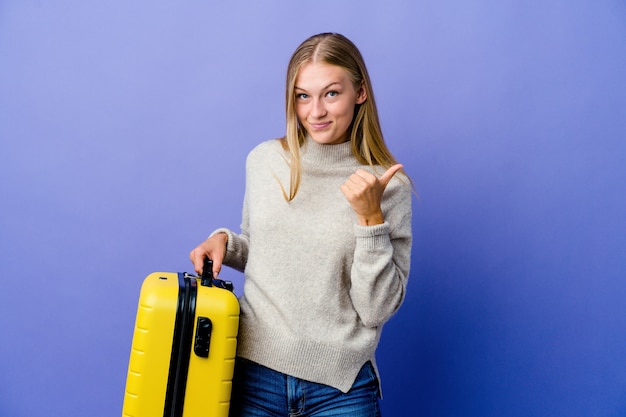 Jovem russa segurando uma mala para viajar, levantando os dois polegares, sorrindo e confiante