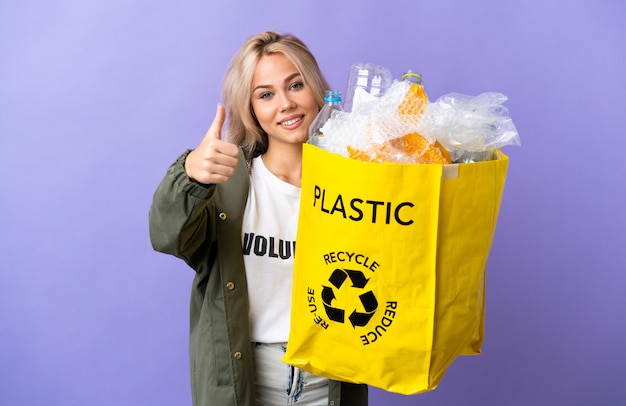 Jovem russa segurando uma sacola de reciclagem cheia de papel para reciclar isolada em roxo com o polegar para cima porque algo bom aconteceu