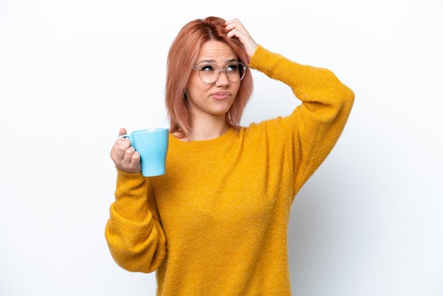 Jovem russa segurando xícara de café isolada em fundo branco com dúvidas e com expressão de rosto confuso