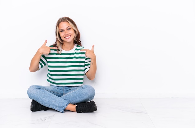 Jovem russa sentada no chão isolada em fundo branco orgulhosa e satisfeita