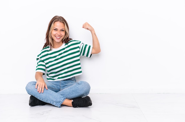 Jovem russa sentada no chão isolada no fundo branco fazendo um gesto forte