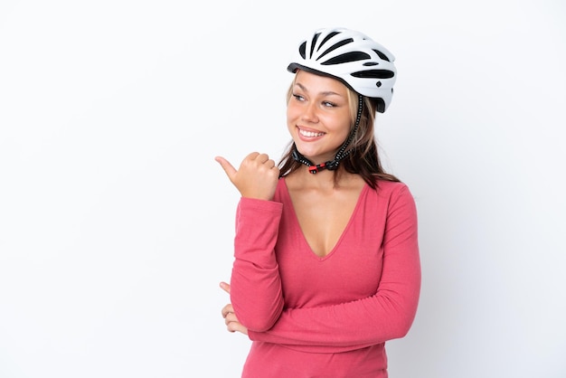 Jovem russa usando um capacete de bicicleta isolado no fundo branco apontando para o lado para apresentar um produto