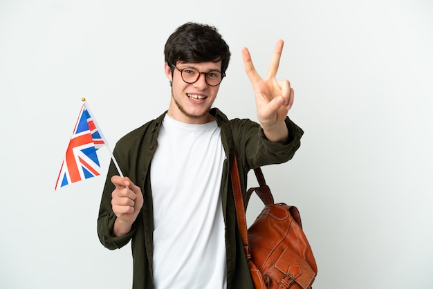 Jovem russo segurando uma bandeira do reino unido, isolada no fundo branco, sorrindo e mostrando o sinal da vitória