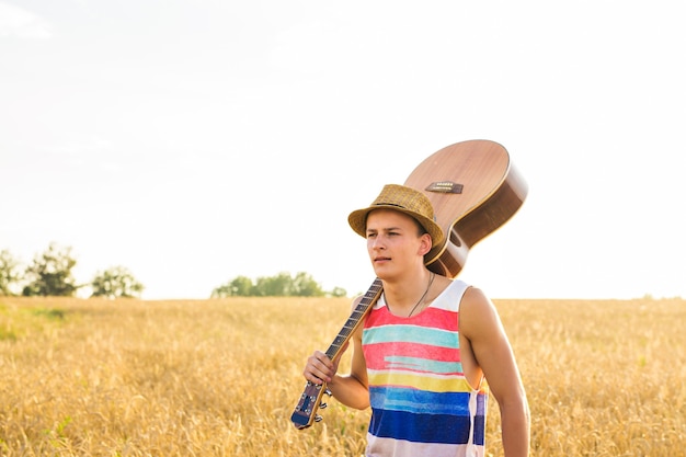 Jovem saindo de casa, cara com violão andando no campo do pôr do sol