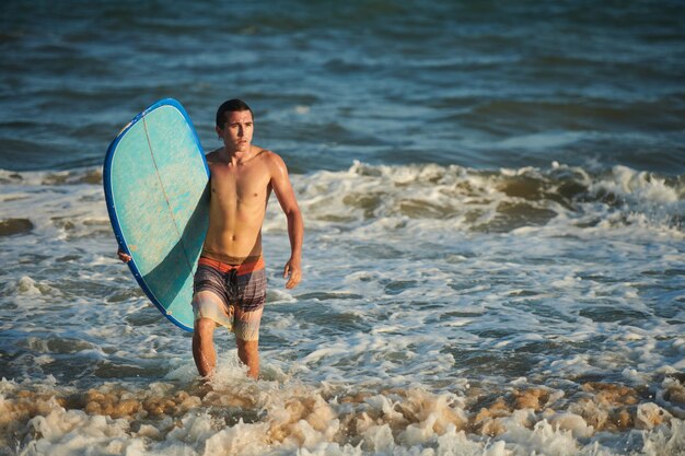 Jovem saindo do oceano depois de surfar no raio de sol poente