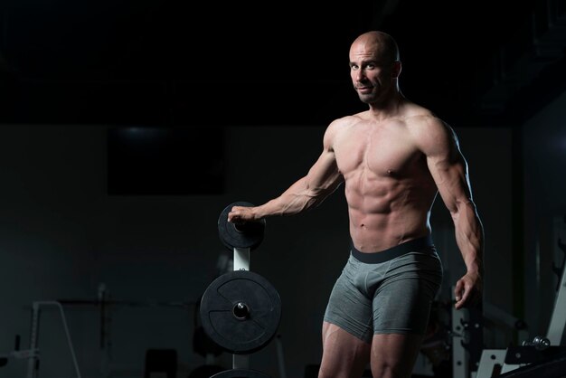 Jovem saudável em pé forte na academia e flexionando os músculos Muscular Atlético Fisiculturista Modelo de fitness posando após exercícios