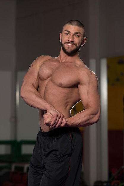 Jovem saudável em pé forte na academia e flexionando os músculos Muscular Atlético Fisiculturista Modelo de fitness posando após exercícios