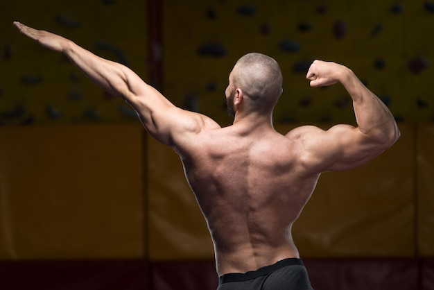 Jovem saudável em pé forte na academia e flexionando os músculos Muscular Atlético Fisiculturista Modelo de fitness posando após exercícios