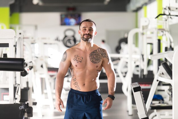 Jovem saudável tatuagem homem de pé forte na academia e flexionando os músculos Muscular Atlético Fisiculturista Fitness Modelo Posando Após Exercícios