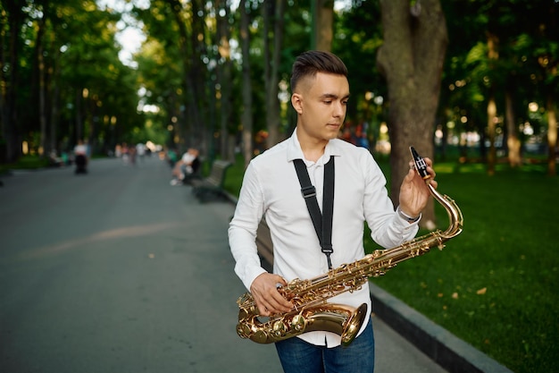 Jovem saxofonista com saxofone em um beco no parque