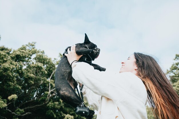 Jovem se divertindo brincando e dançando com seu cachorro bulldog francês em uma imagem de retrato de parque conceito de animal de estimação novo membro da família mulher levando seu cachorro para passear durante um dia ensolarado