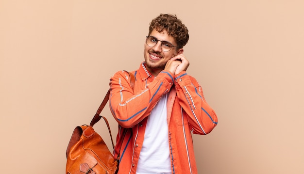 Jovem se sentindo apaixonado e bonito, adorável e feliz, sorrindo romanticamente com as mãos ao lado do rosto. conceito de estudante