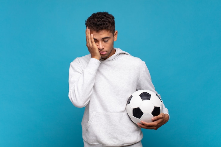 Foto jovem se sentindo entediado, frustrado e com sono após uma tarefa cansativa, enfadonha e tediosa, segurando o rosto com a mão. conceito de futebol