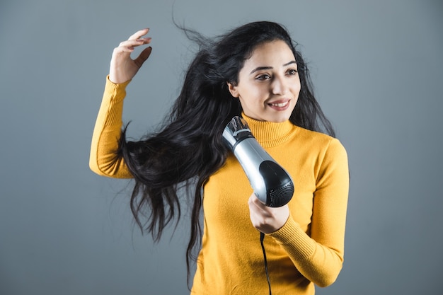 Jovem secador de cabelo de mão em fundo cinza