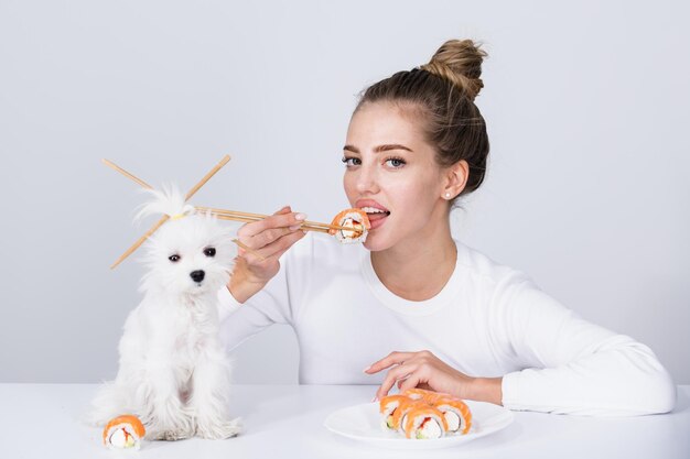 Jovem segura na mão makizushi sushi roll tradicional comida japonesa isolada retrato de estúdio Mulher e cachorrinho com pauzinhos comendo sushi