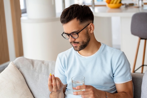 Jovem segura pílulas e copo de água nas mãos Conceito de saúde e medicina paciente toma dose diária de medicamento prescrito sente-se doente antibióticos analgésicos ou antidepressivos Close-up