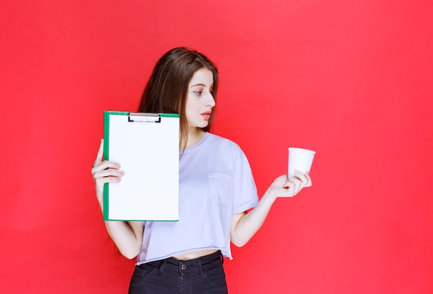 Foto jovem segurando a folha de relatório e oferecendo um copo de bebida.