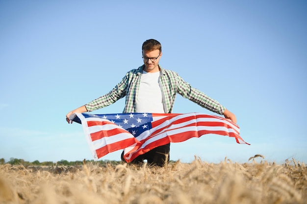 Jovem segurando bandeira americana em pé no campo de trigo