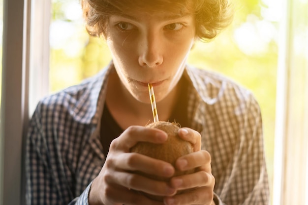 Jovem segurando coco com um canudo e bebendo de perto