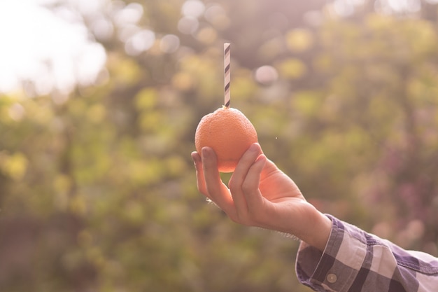 Jovem segurando e bebendo a fruta laranja com túbulo inserido nela