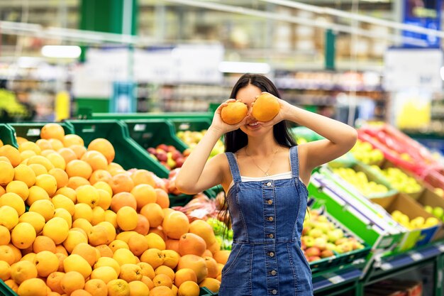 Jovem segurando laranjas nas mãos contra prateleiras com frutas