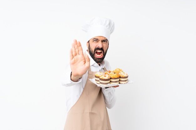 Jovem, segurando o bolo muffin sobre branco isolado, fazendo o gesto de parada e desapontado