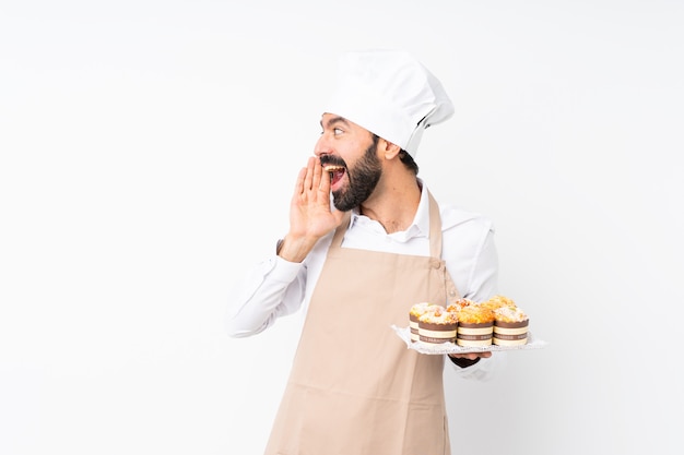 Jovem, segurando o bolo muffin sobre branco isolado gritando com a boca aberta para a lateral