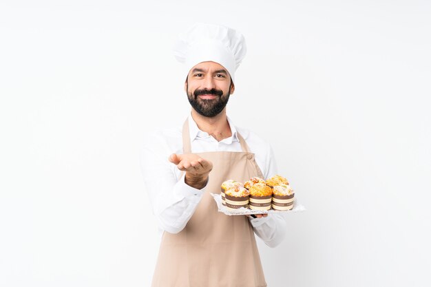 Jovem, segurando o bolo muffin sobre branco isolado segurando copyspace imaginário na palma da mão para inserir um anúncio