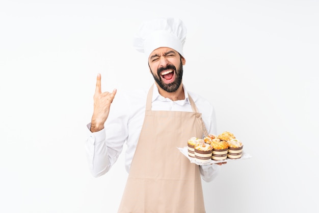 Jovem, segurando o bolo muffin sobre parede branca isolada, fazendo gesto de pedra