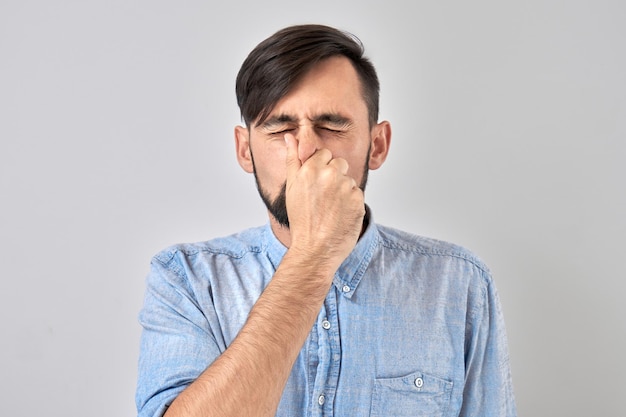 Jovem, segurando o nariz para evitar o cheiro repugnante, belisca o nariz e a boca com os dedos e prende a respiração isolada no fundo branco
